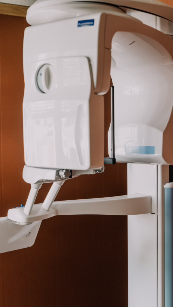 Panoramic dental X-ray machine in a clinic, a large white imaging unit with an adjustable arm and chin rest without a patient present.