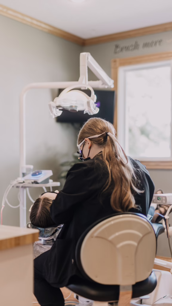 Dentist in a black coat treats a patient in a dental chair under an overhead light